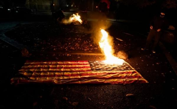 Demonstran anti-Trump melakukan aksi pembakaran bendera Amerika Serikat dalam unjuk rasa yang berujung ricuh di Seattle, Rabu (3/11/2020) malam waktu setempat. (foto: The Sun)