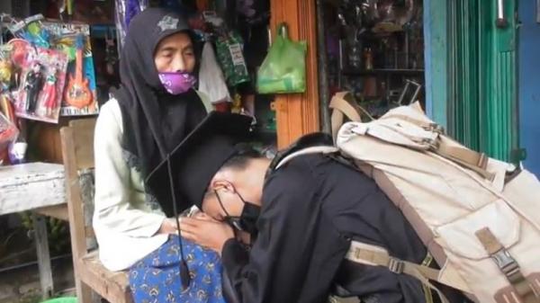 Mochamad Nadif Nasrulloh (23), yang baru mengikuti wisuda virtual di depan makam sang ayah bersujud di hadapan ibunya di Banjarnegara, Jateng, Selasa (24/11/2020). (Foto: iNews/Widodo)