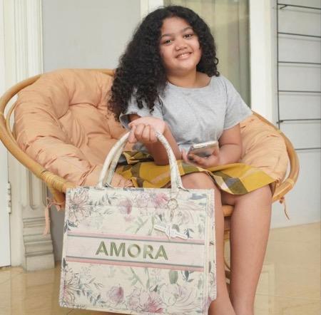 Ariannha Amora Lemos 3 Amora dengan tas bertuliskan namanya.