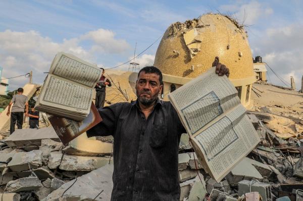 Seorang pria Palestina memegang mushaf Alquran di depan sebuah masjid yang hancur di Kota Khan Yunis, selatan Jalur Gaza, menyusul serangan udara Israel pada hari kedua konflik yang sedang berlangsung antara Israel dan kelompok militan Palestina Hamas, Minggu (8/10/2023). (Foto: Reuters)
