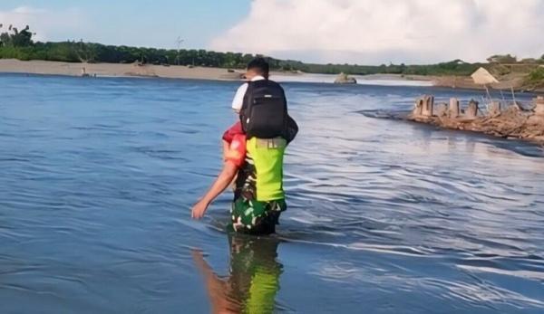 Babinsa Tni Ad Babinsa Posramil 12/Ptr Kodim 0105/Abar Serka Zulfan memanggul pelajar SD Negeri Meunuang Kinco menyeberangi Sungai Aceh Barat. (Foto Dispenad).